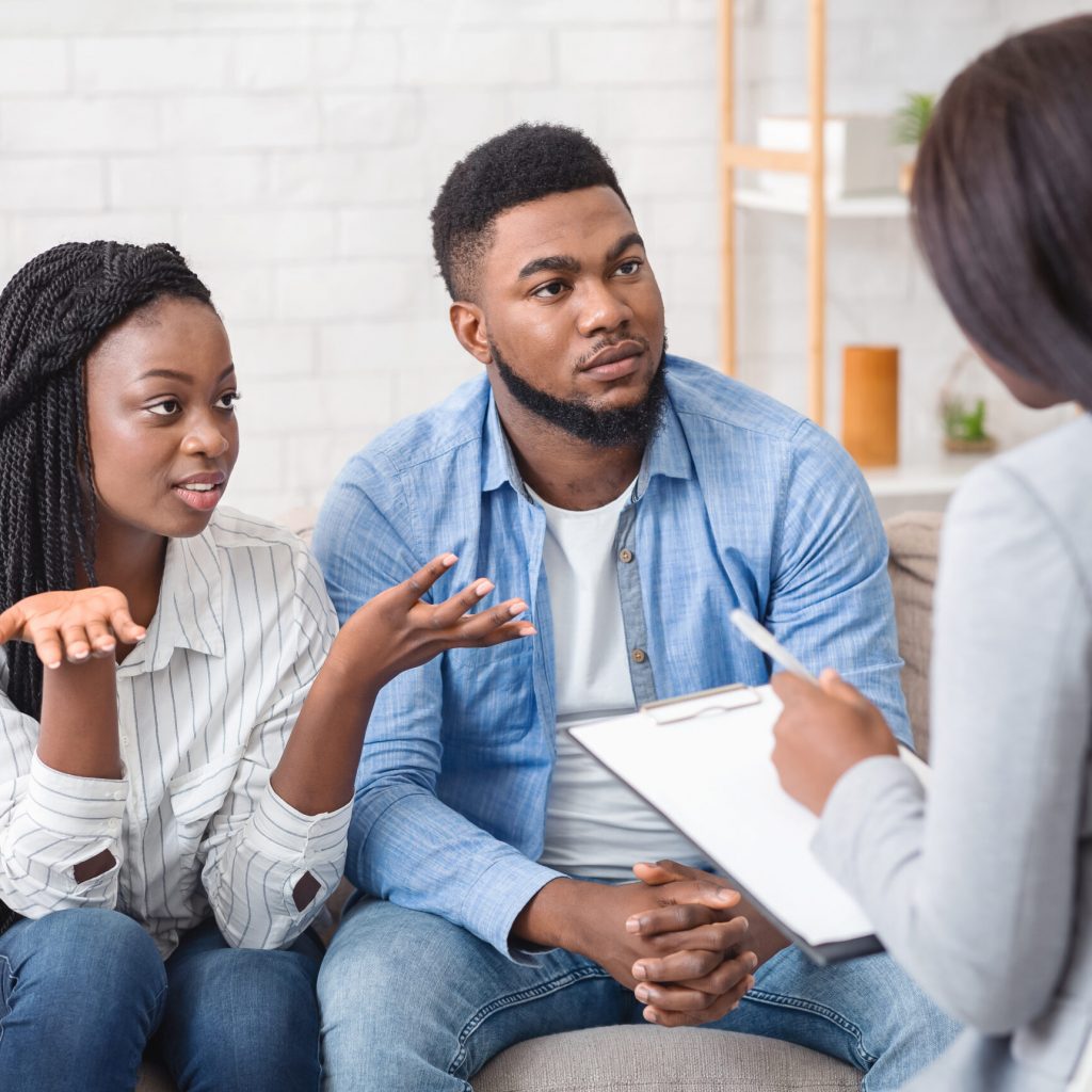 Marital psychotherapy concept. Young afro couple with relationship problems sitting at therapy session with psychologist